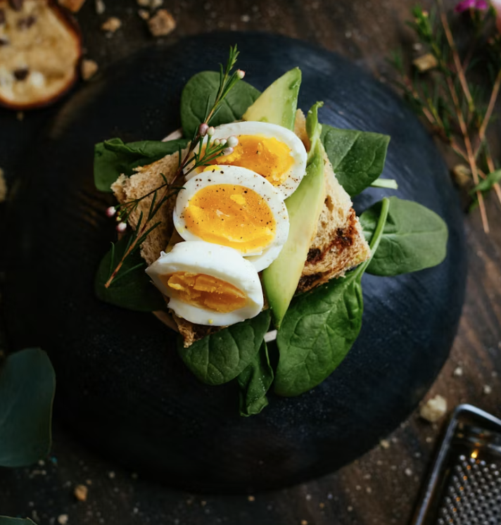 Soft boiled eggs and avocado on toast with spinach, plated on a dark slate board